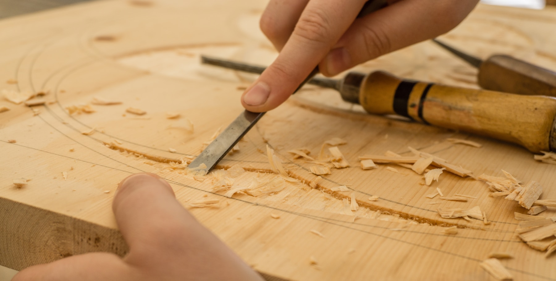 Hände führen den Meißel über eine Holzplatte
